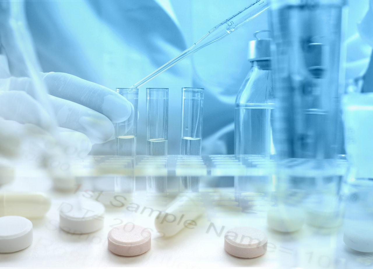 Eine Person pipettiert eine Flüssigkeit in drei Reagenzgläser. Im Vordergrund sind verschiedene Tabletten abgebildet
