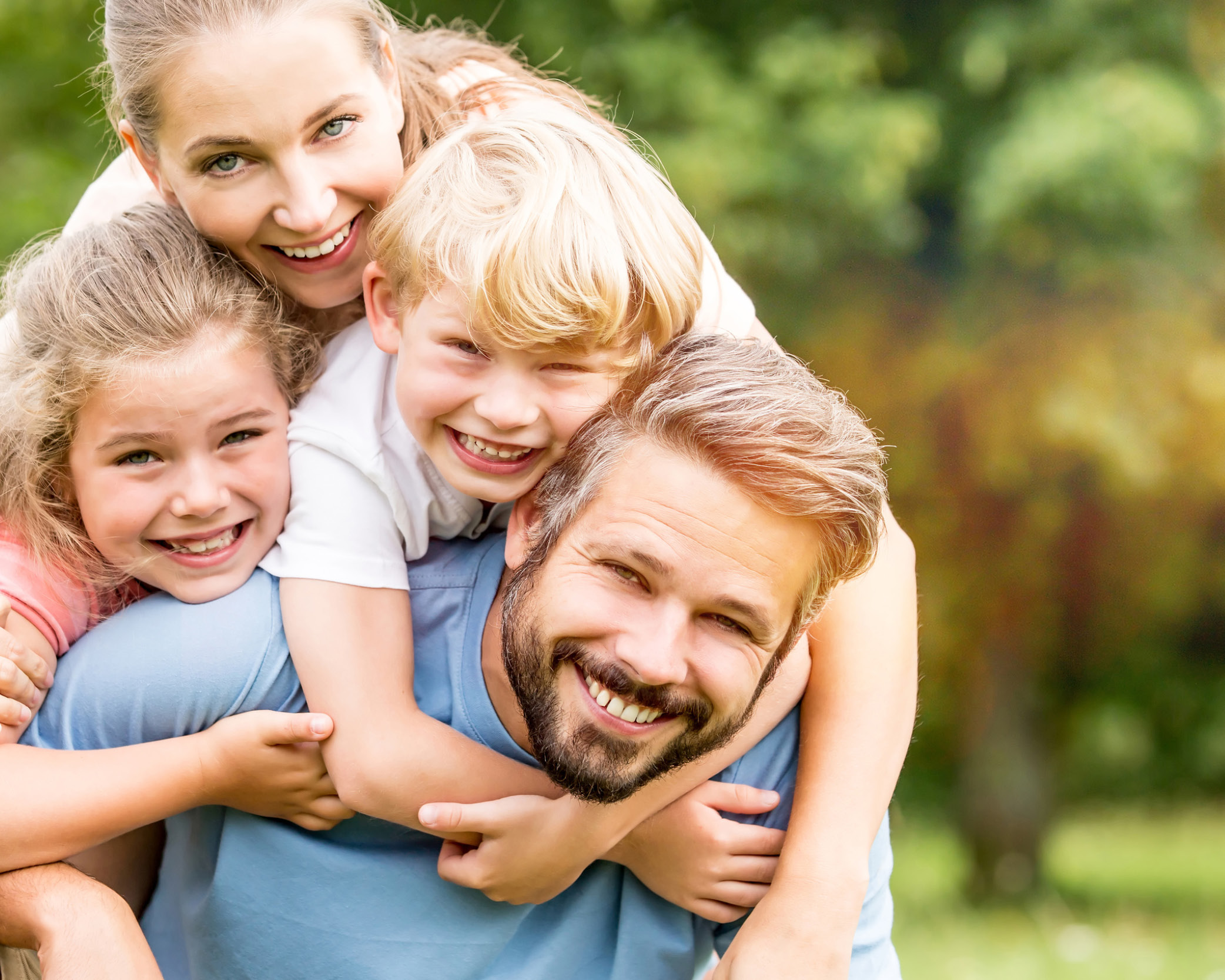 Eine Familie mit zwei Kindern lacht eng umschlungen in die Kamera