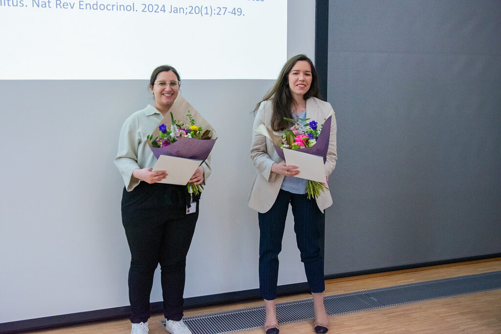 Zwei Frauen stehen nebeneinander und halten Blumensträuße sowie Urkunden in den Händen.