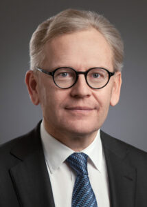 Ein Professor mit Brille und Anzug, der in die Kamera schaut. Er hat graue Haare und trägt eine Krawatte.